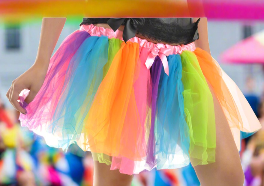 model wearing a rainbow colored tulle tutu skirt with elastic waistband featuring a light pink satin finish and front bow.